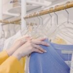 Hands selecting colorful sweaters on a clothing rack inside a modern boutique.